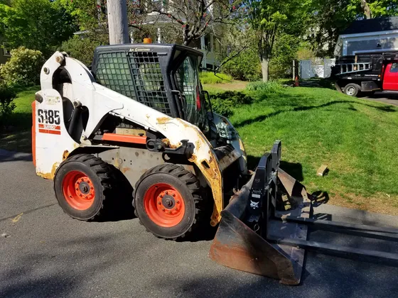 Bobcat S185 Turbo wheeled skid-steer loader with a grading attachment; the S185 badge is visible.