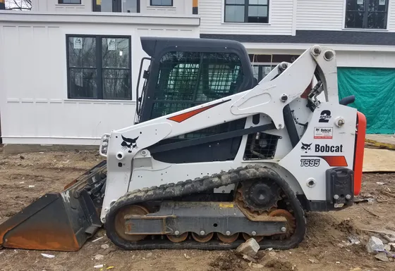 Side view of a Bobcat T595 compact track loader with a bucket at a building site.