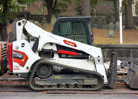 Bobcat T740 compact track loader with pallet forks beside a cemetery.