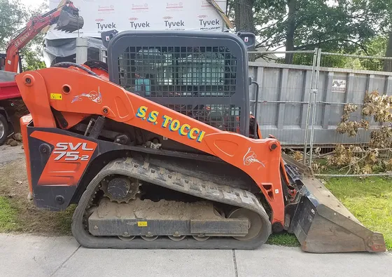 Side view of a Kubota SVL75-2 with a bucket at a construction site; the model badge is visible.